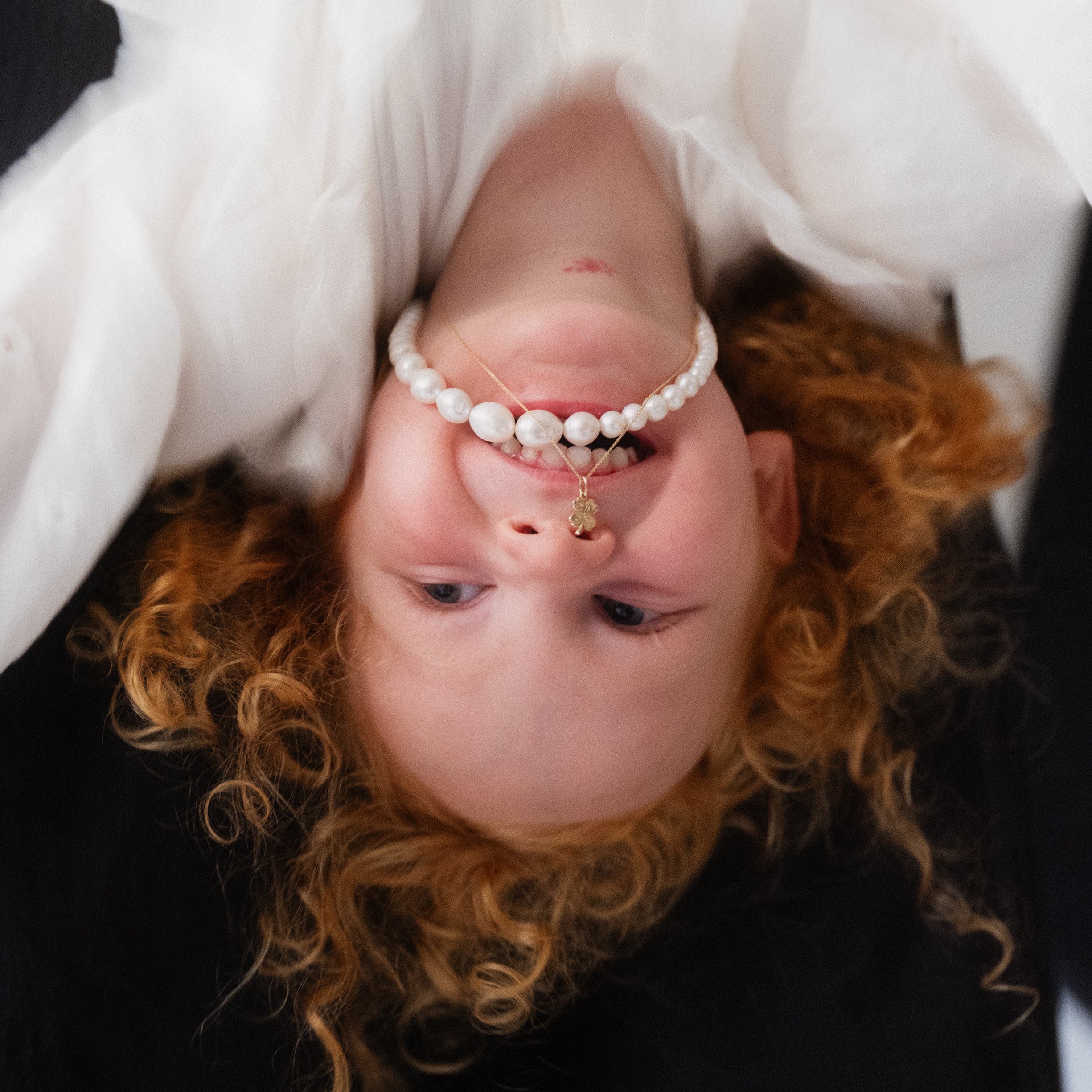 A person wearing a white dress and a gold-colored necklace with a lucky clover-shaped pendant.